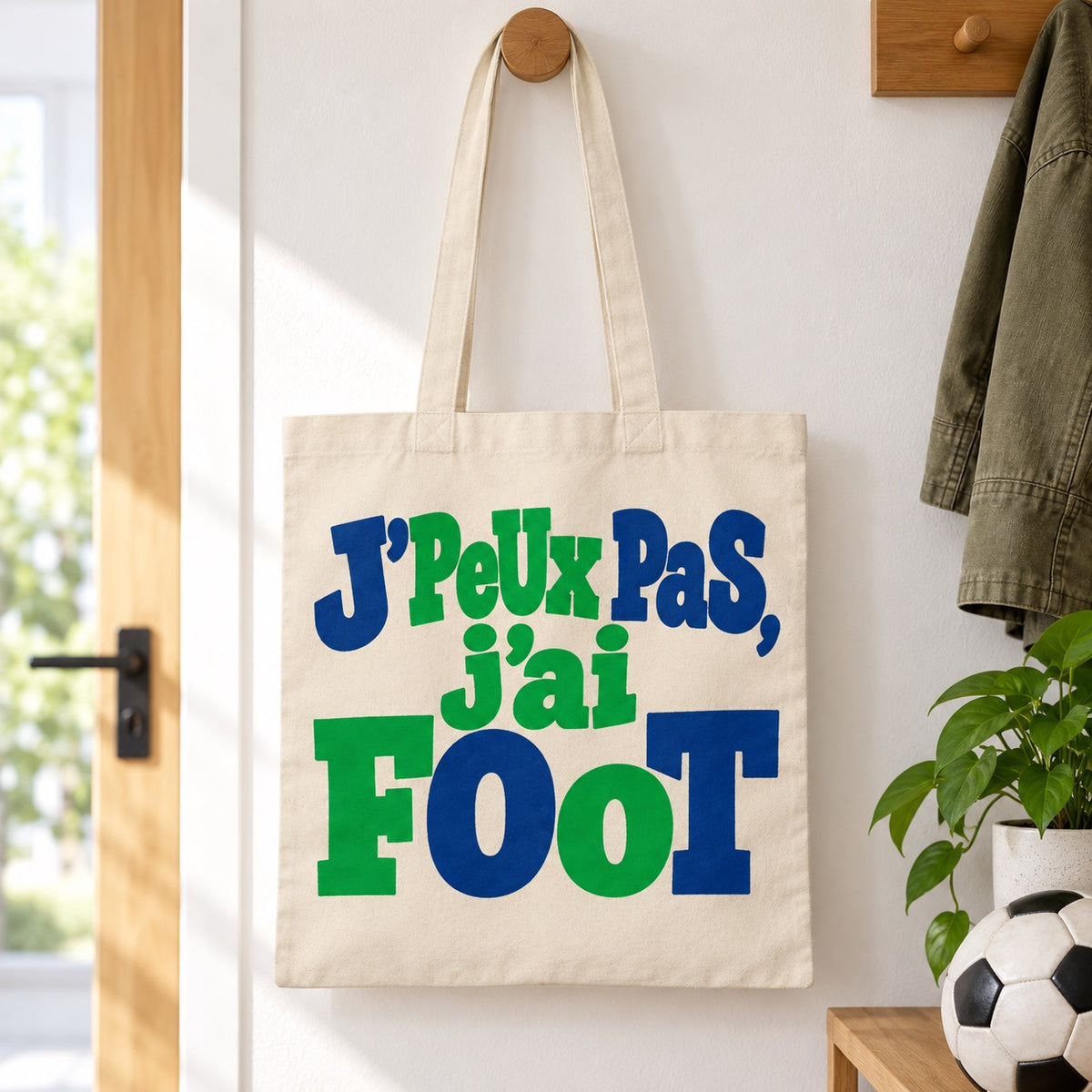 Tote bag « J'peux pas, j'ai foot » Essentiel suspendu à une patère dans une entrée