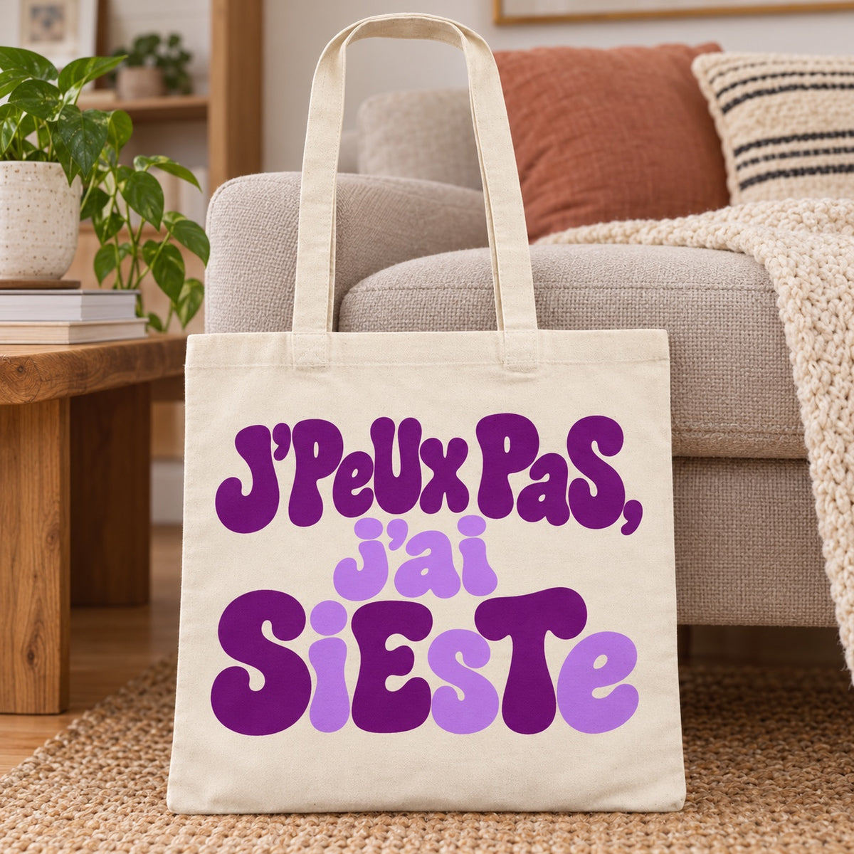 Tote bag « J'peux pas, j'ai sieste » Essentiel posé sur un canapé à côté d'un plaid en grosse maille