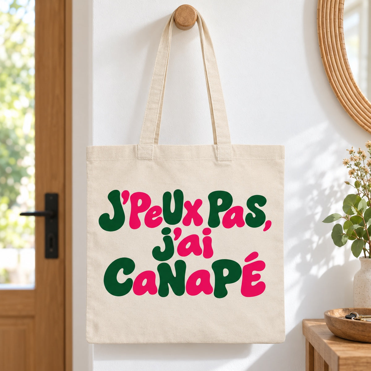 Tote bag « J'peux pas, j'ai canapé » Essentiel suspendu à une patère dans une entrée