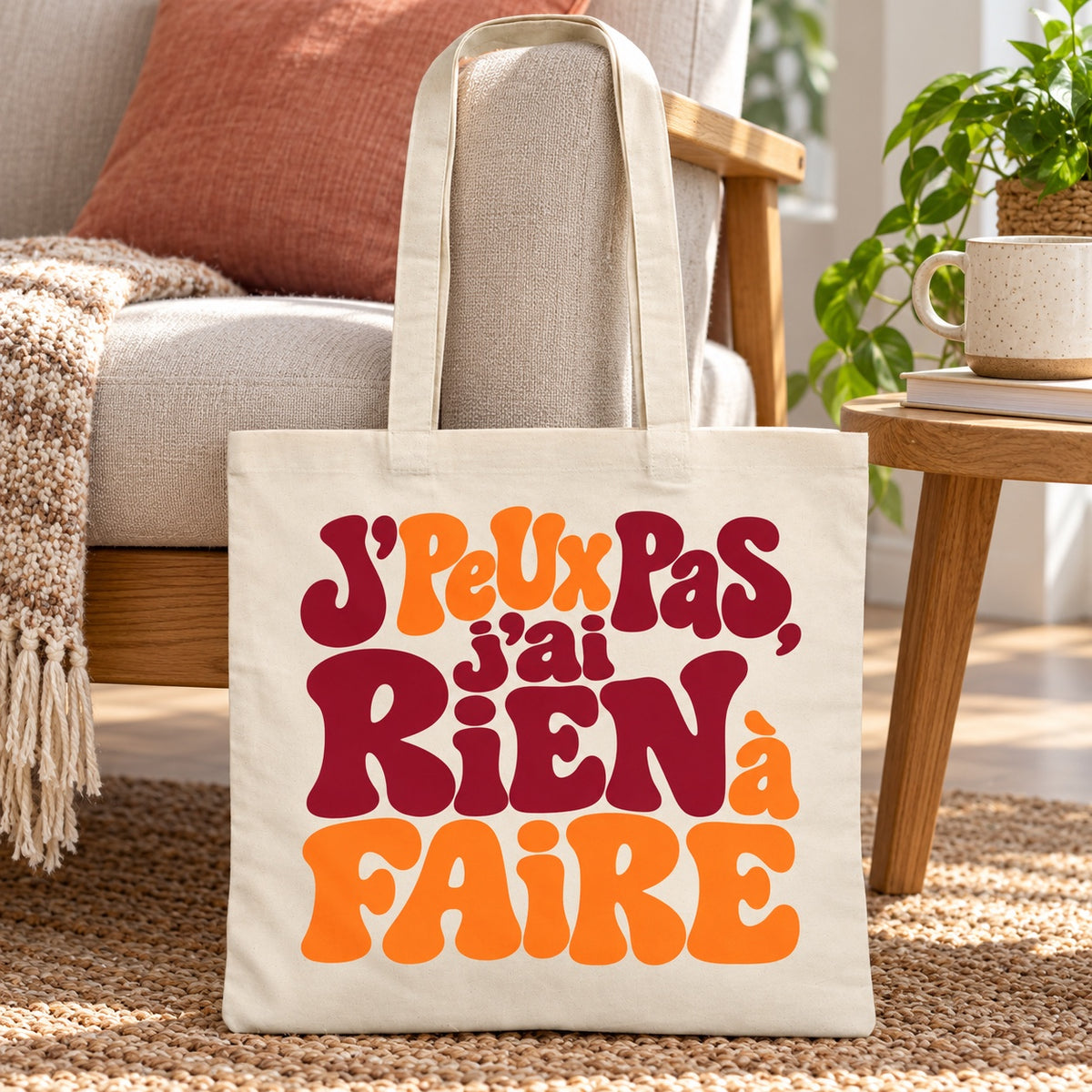 Tote bag « J'peux pas, j'ai rien à faire » Essentiel appuyé contre un fauteuil près d'un plaid