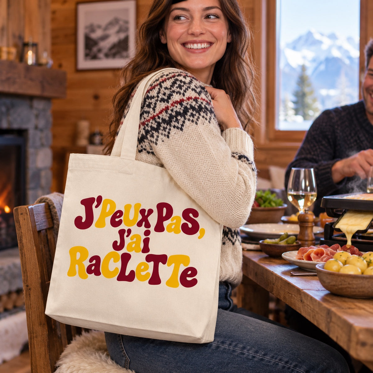 Tote bag « J'peux pas, j'ai raclette » Premium porté à l'épaule dans un chalet de montagne pendant une soirée raclette