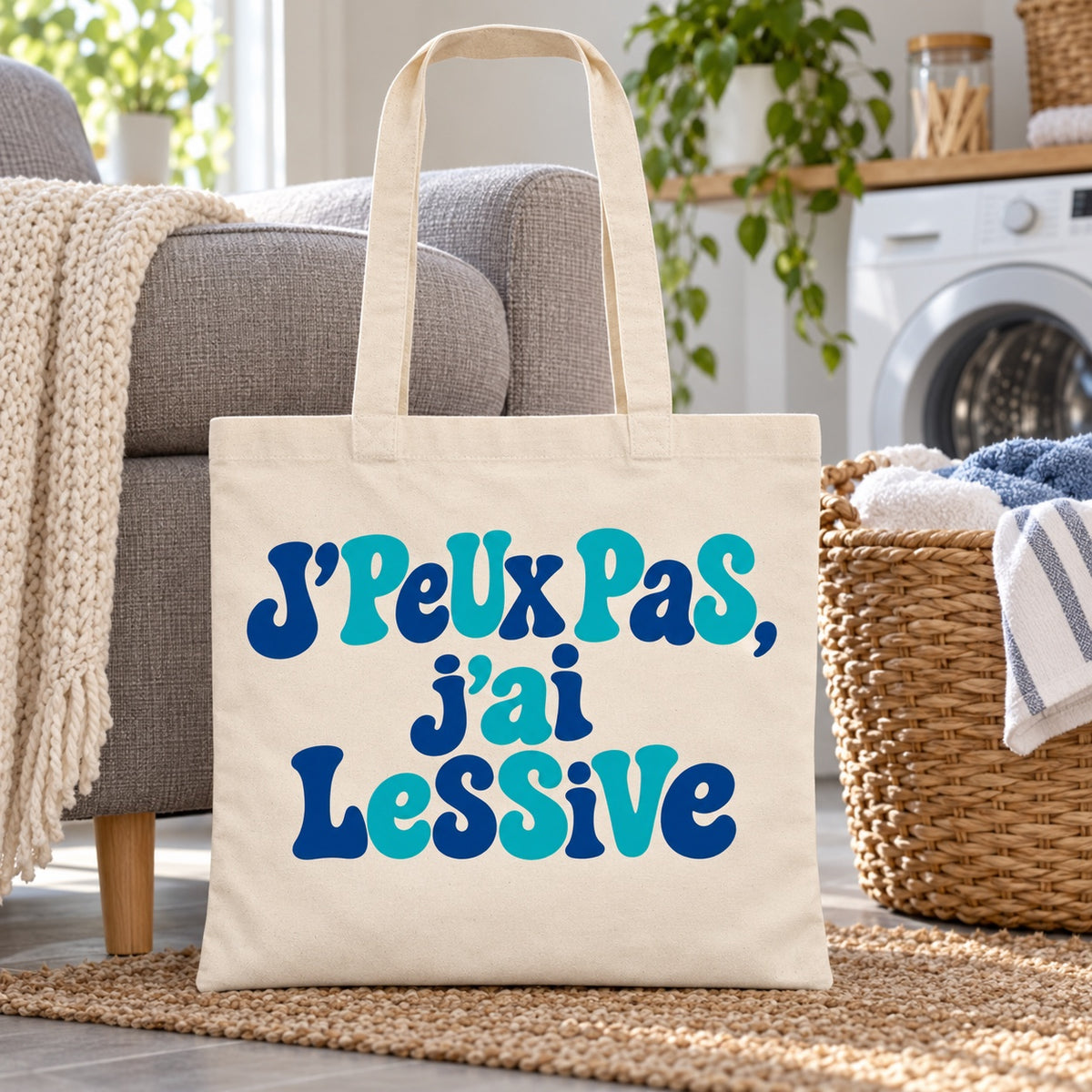 Tote bag « J'peux pas, j'ai lessive » Essentiel appuyé contre un fauteuil près d'une machine à laver