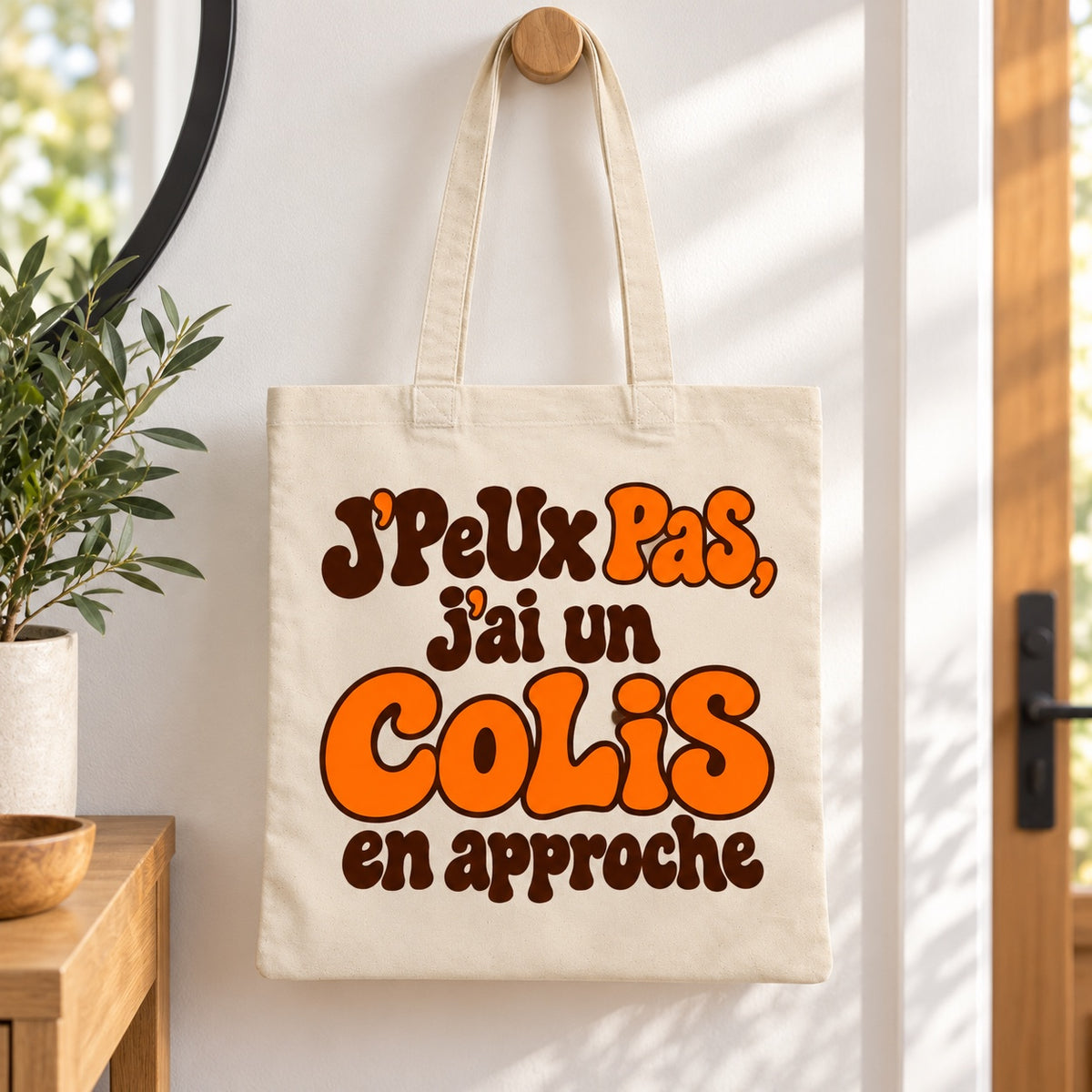 Tote bag « J'peux pas, j'ai un colis en approche » Essentiel suspendu à une patère dans une entrée