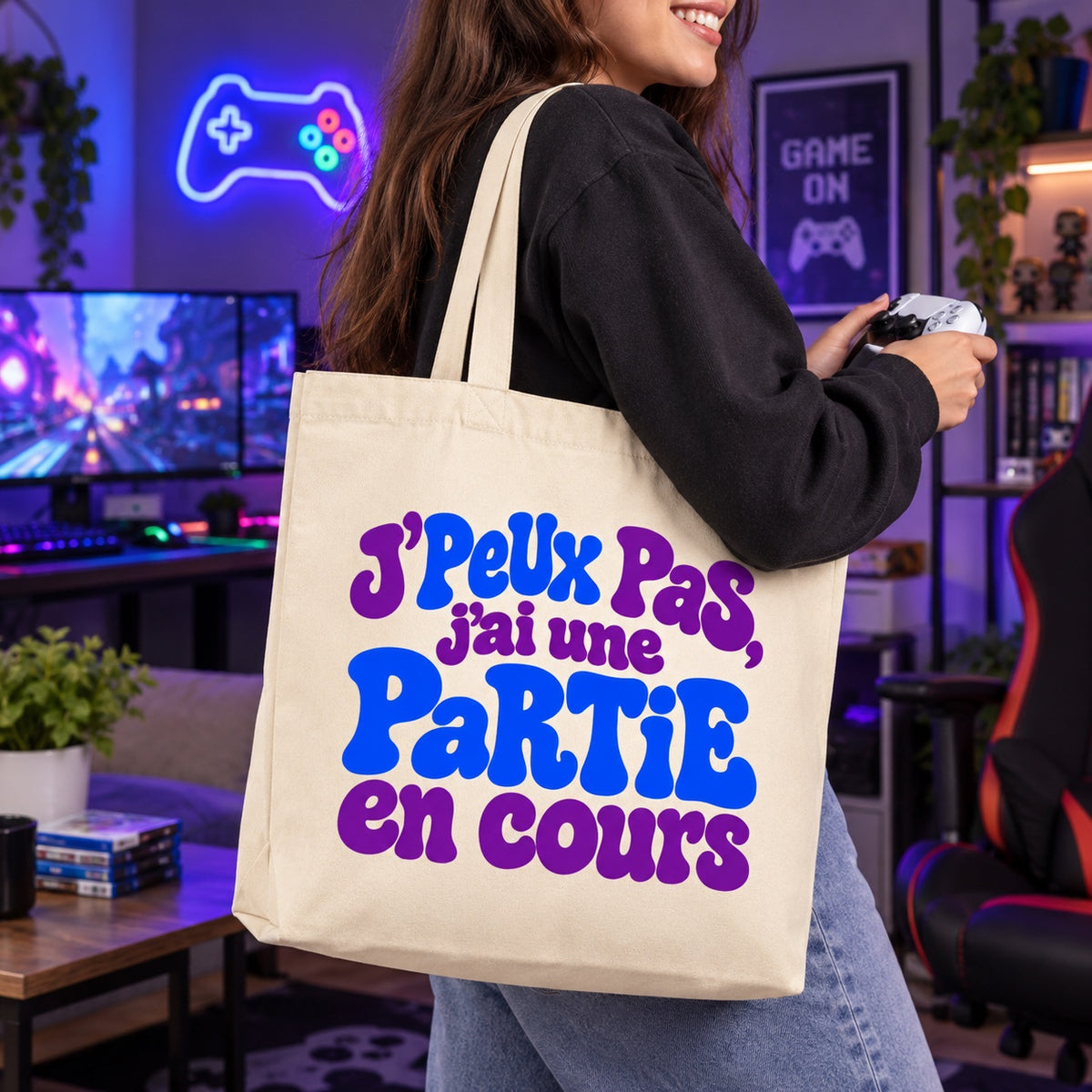 Tote bag « J'peux pas, j'ai une partie en cours » Premium porté à l'épaule dans une salle de jeux aux néons