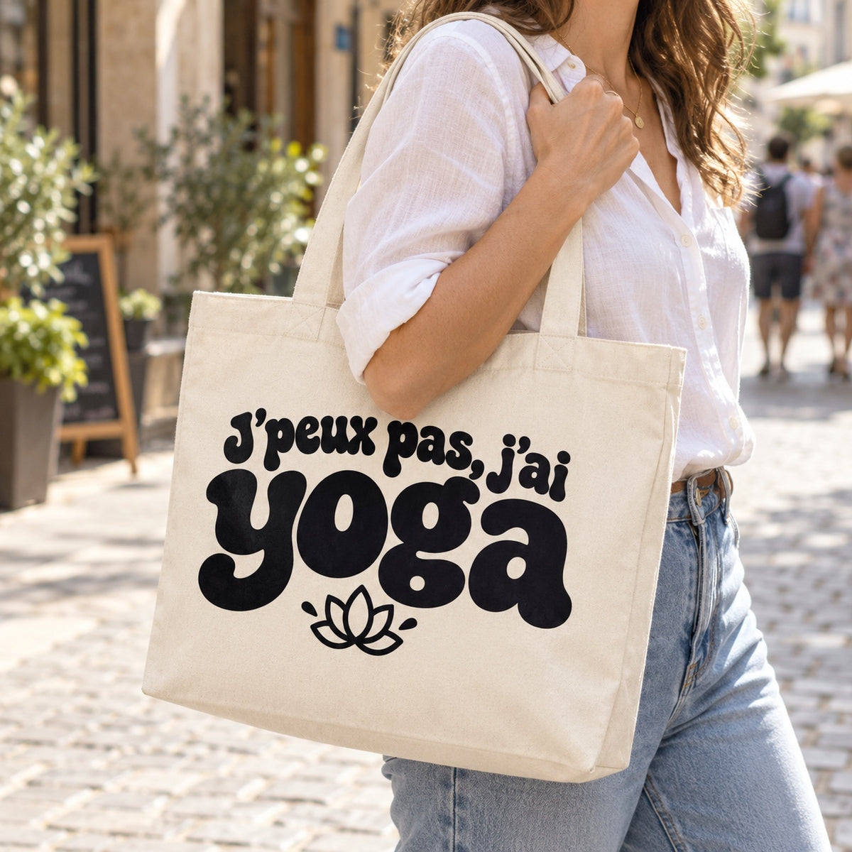 Tote bag « J'peux pas, j'ai yoga » Premium porté à l'épaule dans une rue piétonne ensoleillée
