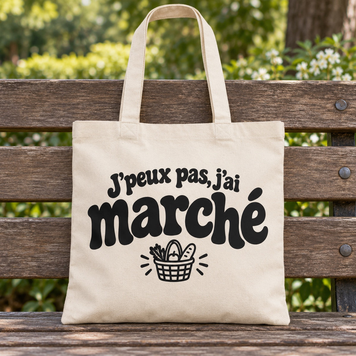 Tote bag « J'peux pas, j'ai marché » Essentiel posé sur un banc en bois dans un jardin
