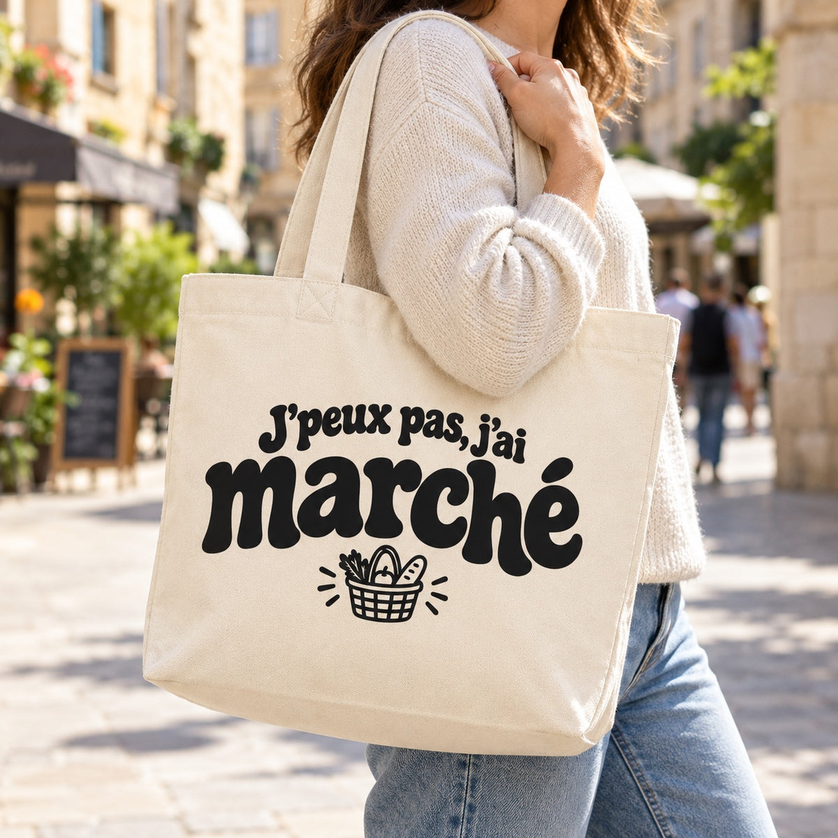 Tote bag « J'peux pas, j'ai marché » Premium porté à l'épaule dans une rue piétonne ensoleillée