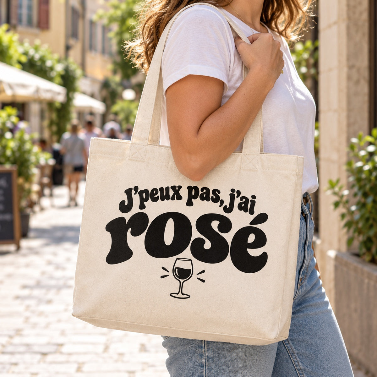 Tote bag « J'peux pas, j'ai rosé » Premium porté à l'épaule dans une rue piétonne ensoleillée