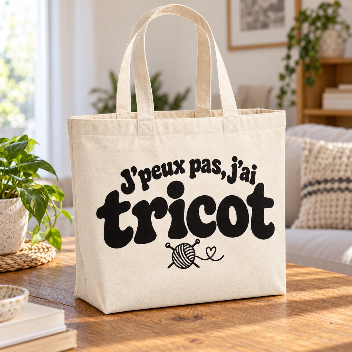 Tote bag « J'peux pas, j'ai tricot » Premium posé sur une table en bois dans un salon lumineux