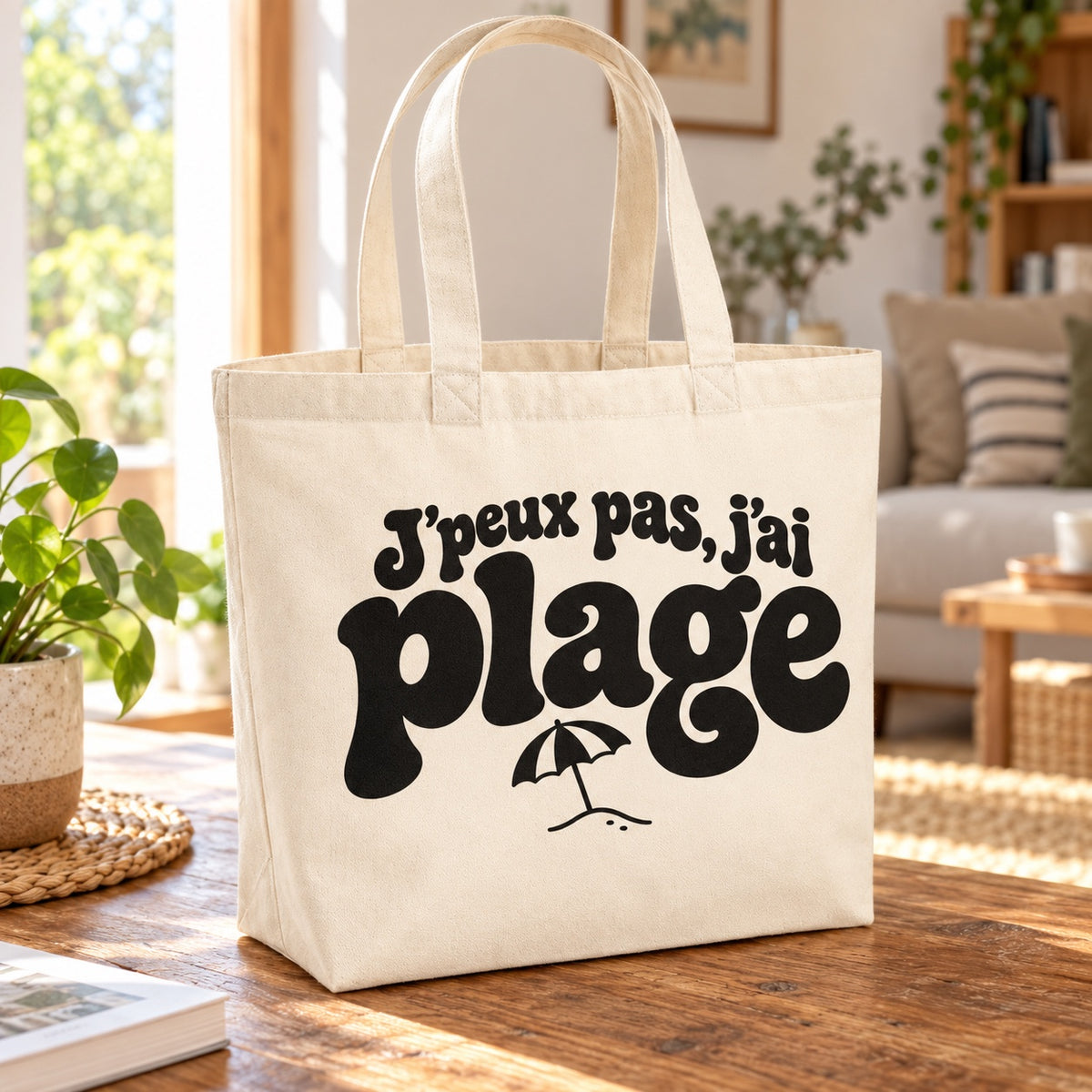 Tote bag « J'peux pas, j'ai plage » Premium posé sur une table en bois dans un salon lumineux