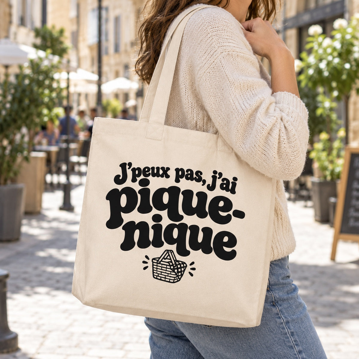 Tote bag « J'peux pas, j'ai pique-nique » Premium porté à l'épaule dans une rue piétonne ensoleillée