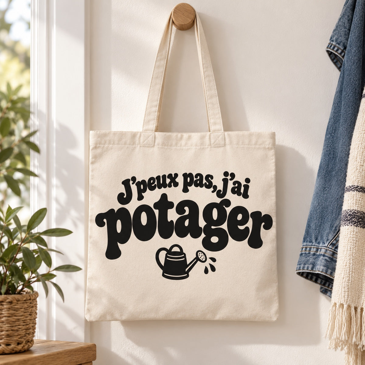 Tote bag « J'peux pas, j'ai potager » Essentiel suspendu à une patère dans une entrée lumineuse