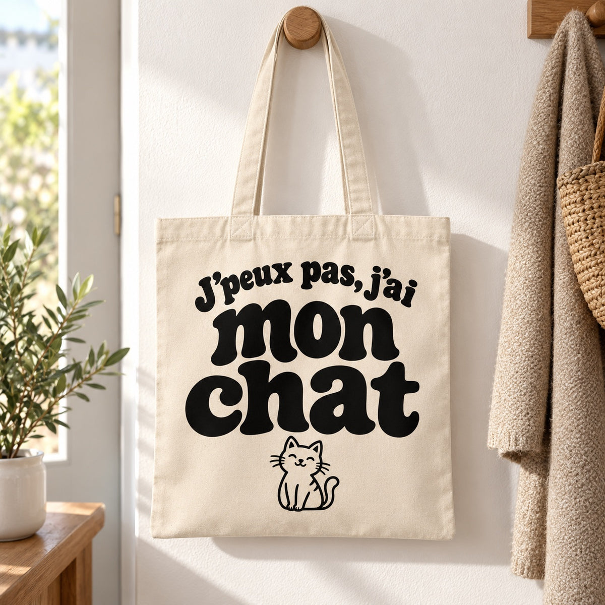 Tote bag « J'peux pas, j'ai mon chat » Essentiel suspendu à une patère dans une entrée lumineuse
