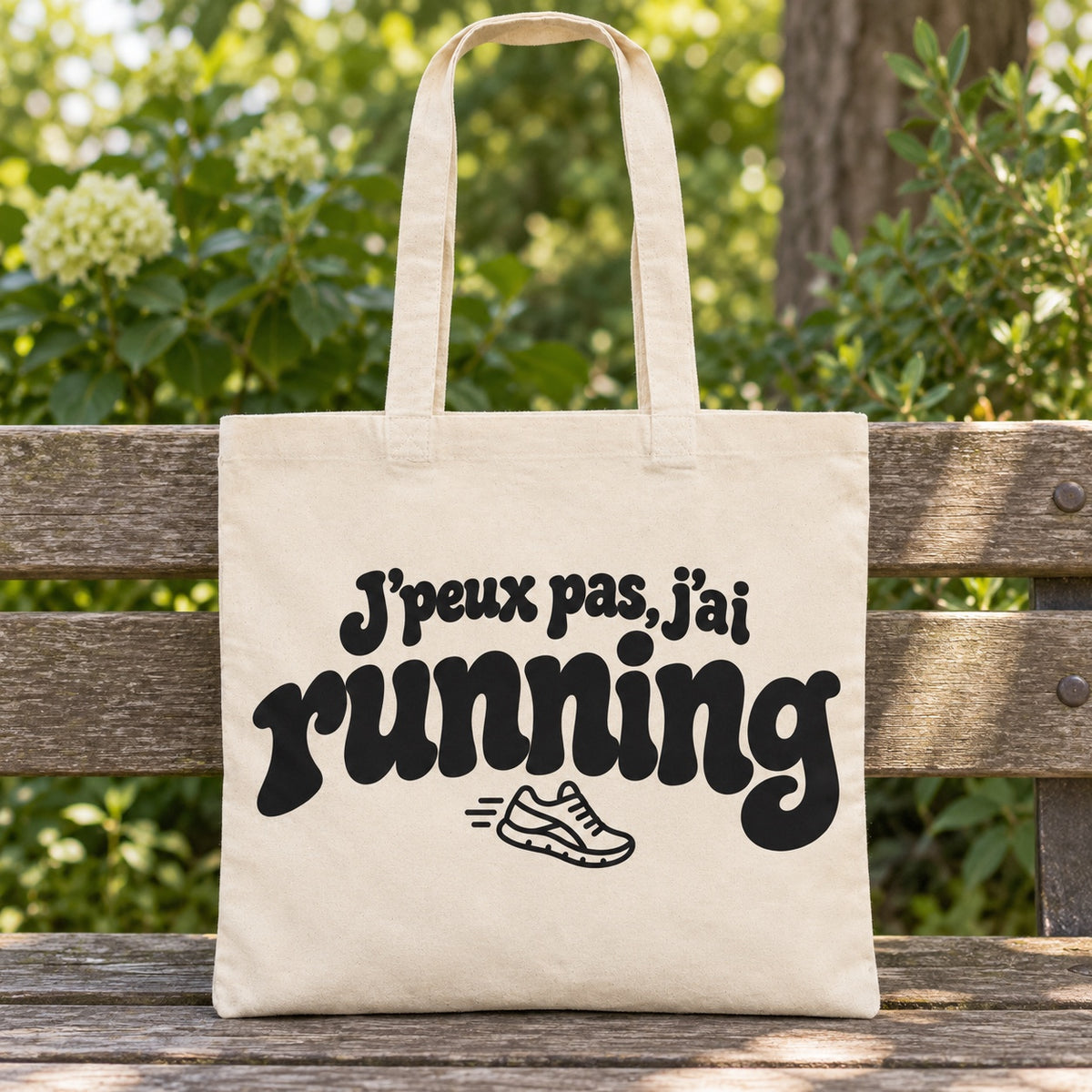 Tote bag « J'peux pas, j'ai running » Essentiel posé sur un banc en bois dans un jardin