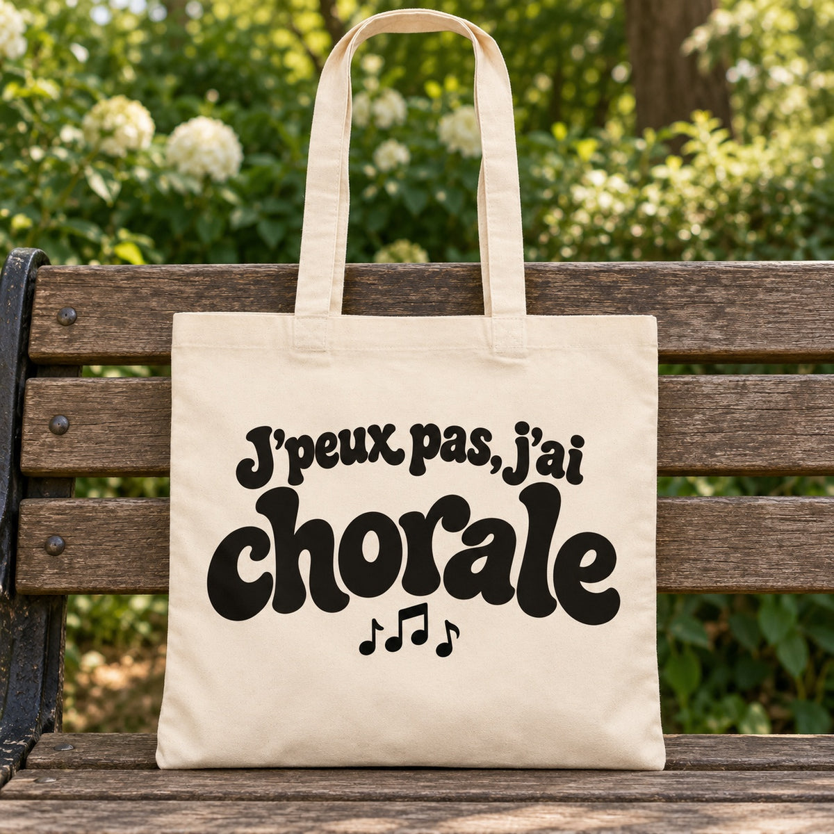 Tote bag « J'peux pas, j'ai chorale » Essentiel posé sur un banc en bois dans un jardin