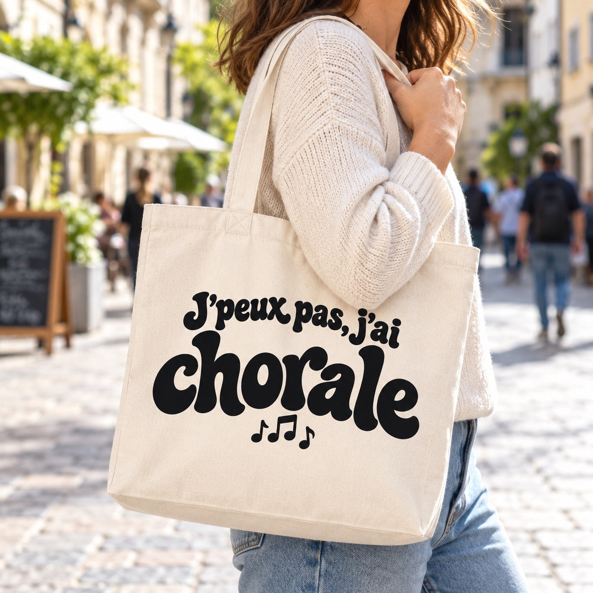 Tote bag « J'peux pas, j'ai chorale » Premium porté à l'épaule dans une rue piétonne ensoleillée