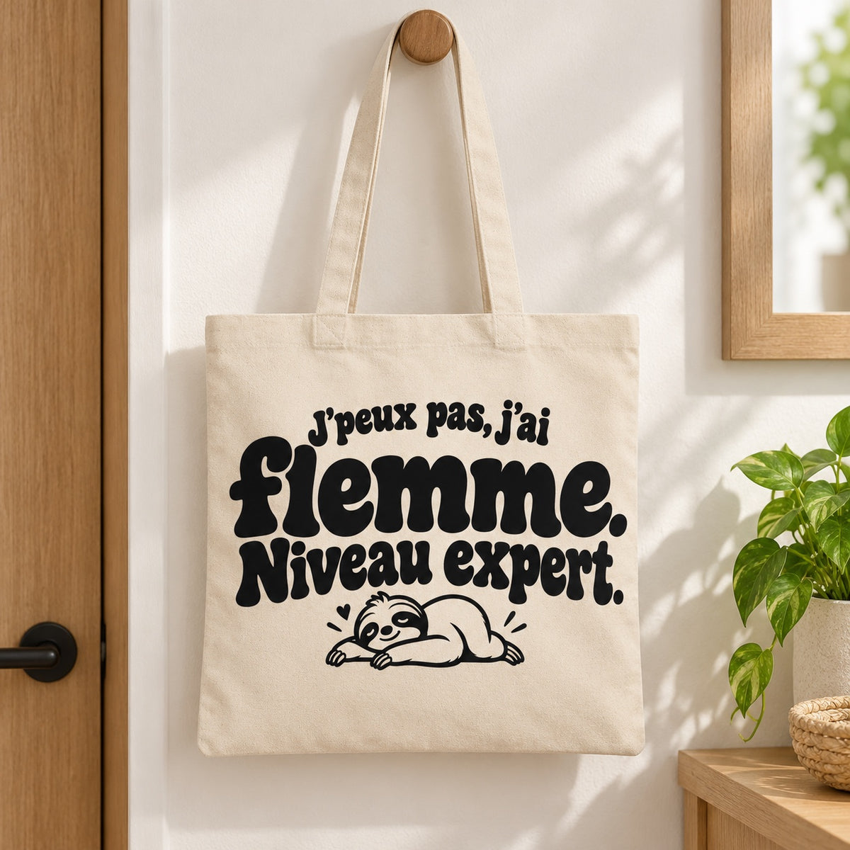 Tote bag « J'peux pas, j'ai flemme. Niveau expert. » Essentiel suspendu à une patère dans une entrée lumineuse