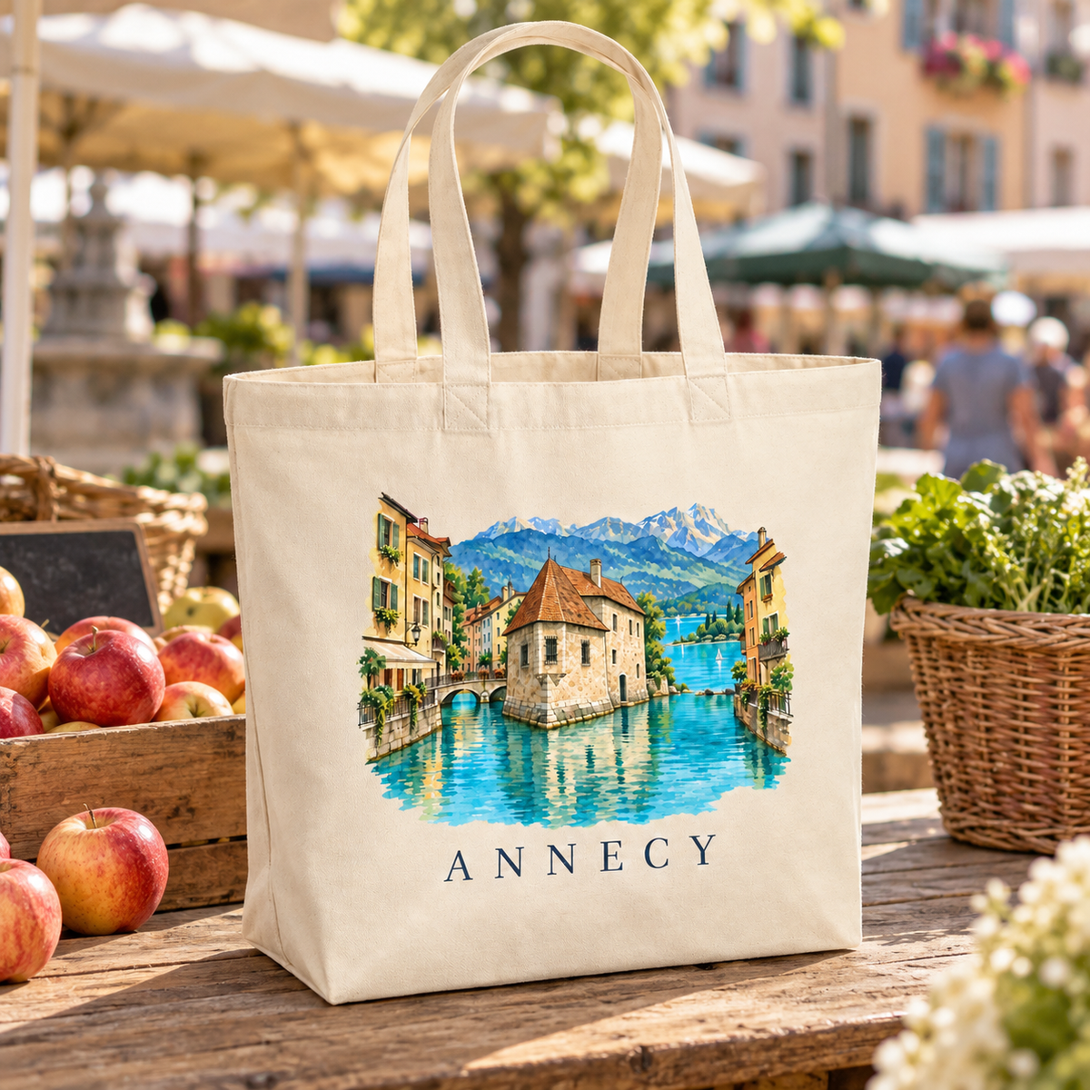 Tote bag Annecy Premium posé sur un étal du marché de la vieille ville, entre paniers de pommes et fleurs