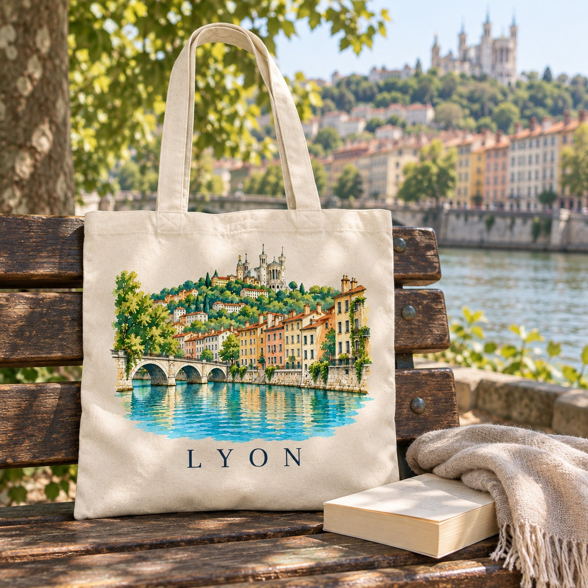Tote bag Lyon Essentiel posé sur un banc en bois face à la Saône et aux façades colorées des quais