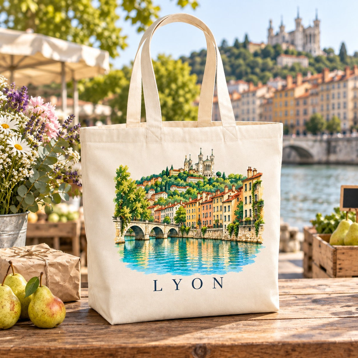 Tote bag Lyon Premium posé sur un étal de marché avec des poires et des fleurs, colline de Fourvière en arrière-plan