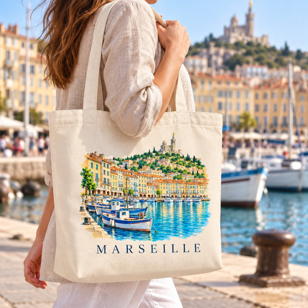 Tote bag Marseille Premium porté à l'épaule sur le quai du Vieux-Port, Notre-Dame de la Garde en arrière-plan