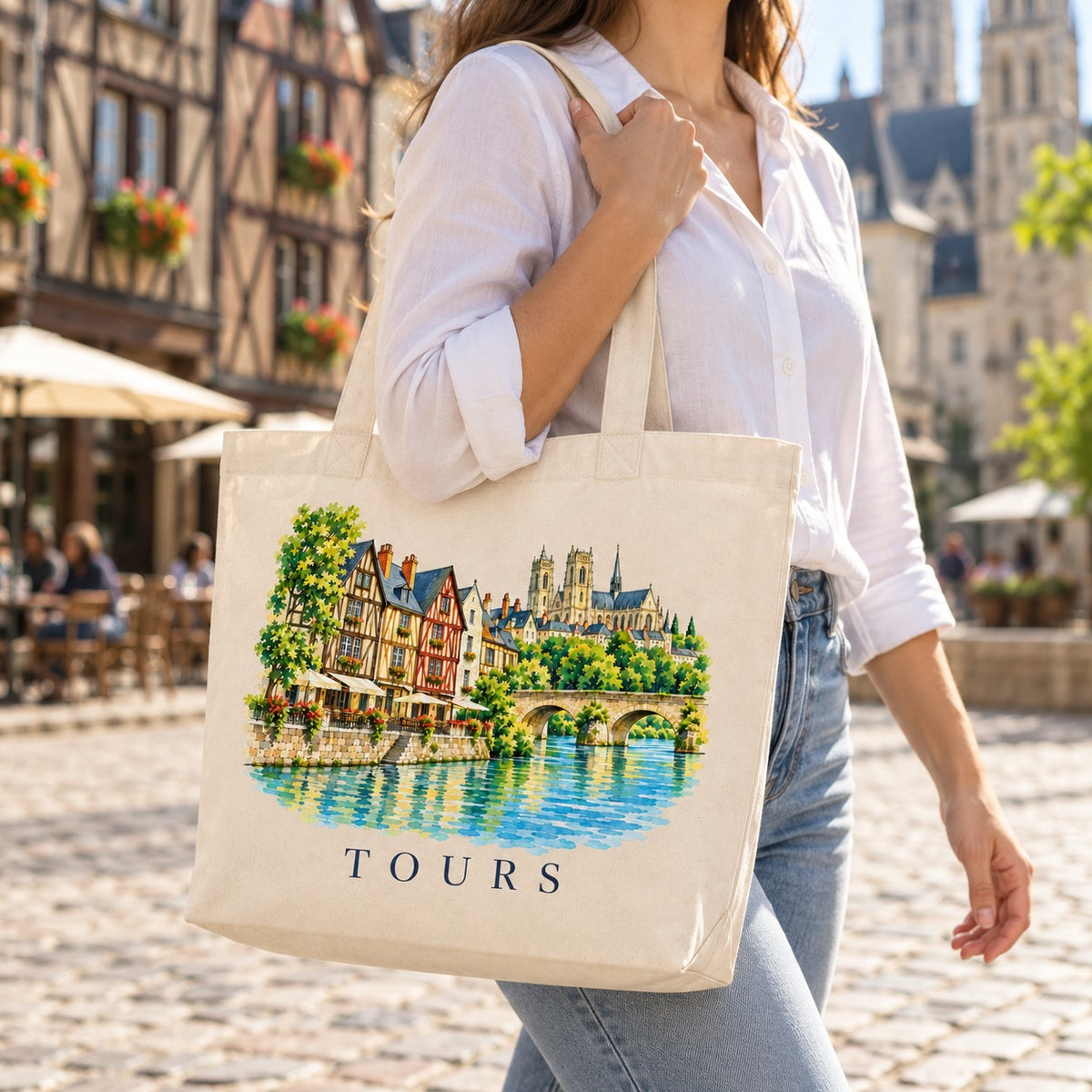 Tote bag Tours Premium porté à l'épaule sur la place Plumereau, maisons à pans de bois en arrière-plan