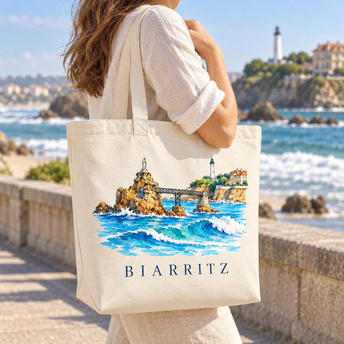 Tote bag Biarritz Premium porté à l'épaule sur la promenade face à l'océan, rocher de la Vierge en arrière-plan