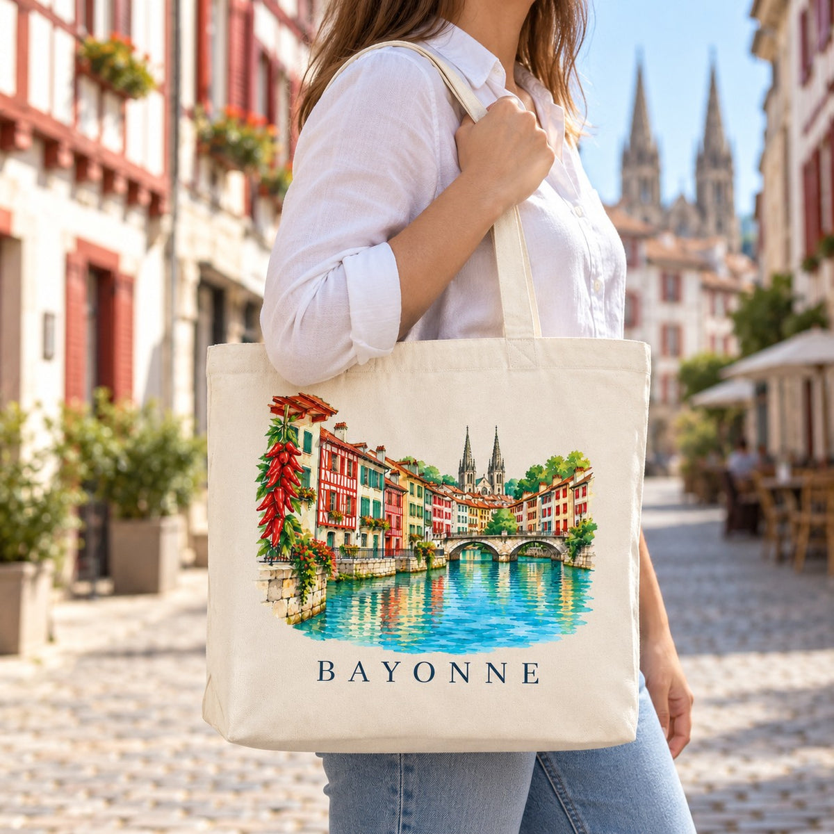 Tote bag Bayonne Premium porté à l'épaule dans une rue aux façades basques colorées