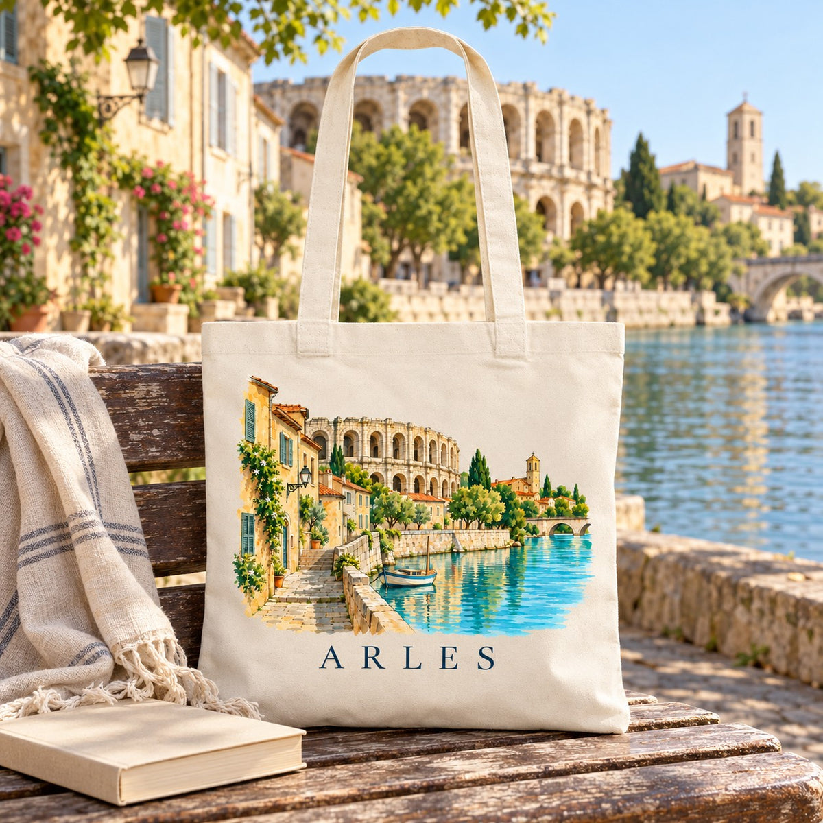 Tote bag Arles Essentiel posé sur un banc au bord du Rhône, avec un livre et un plaid