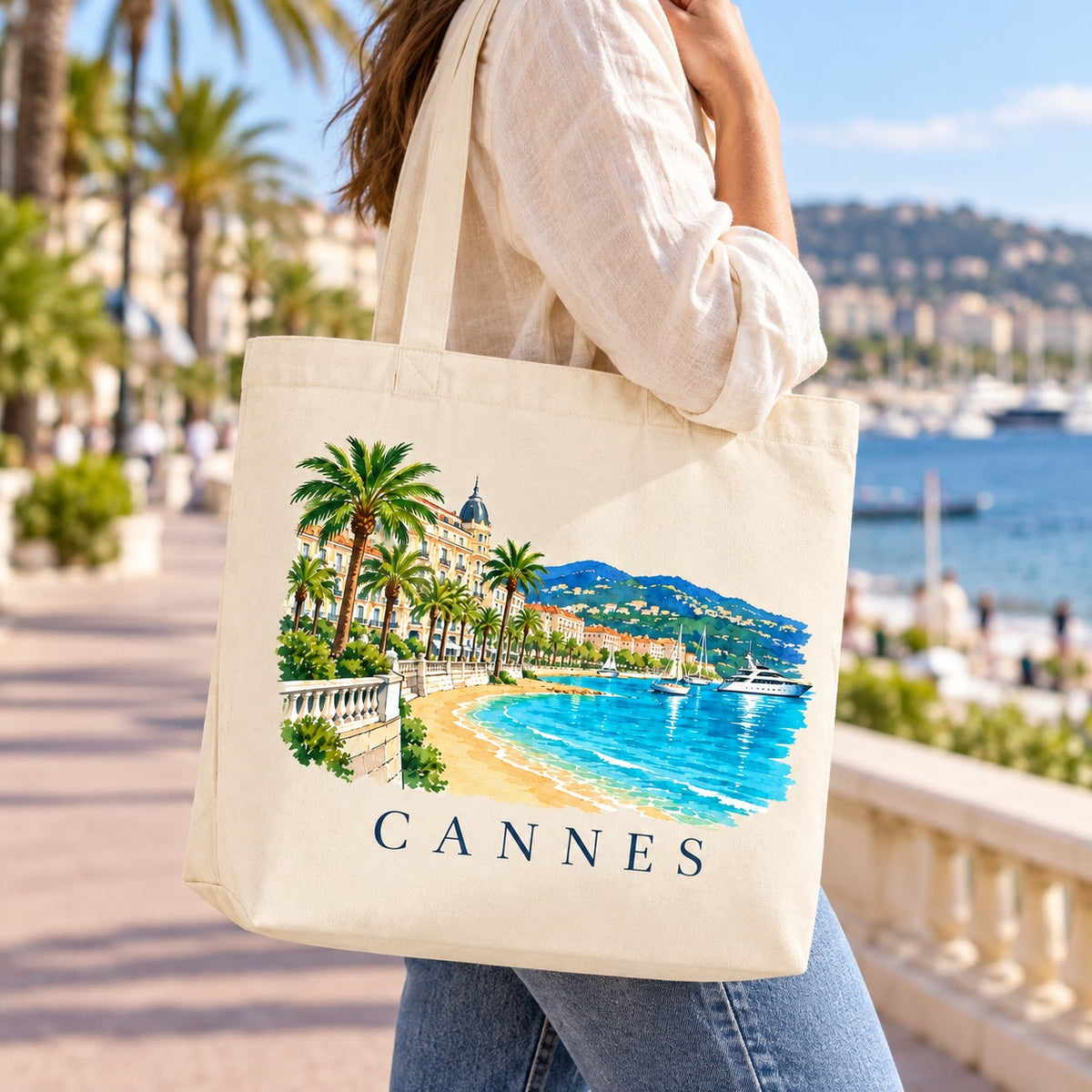 Tote bag Cannes Premium porté à l'épaule sur la Croisette, baie en arrière-plan
