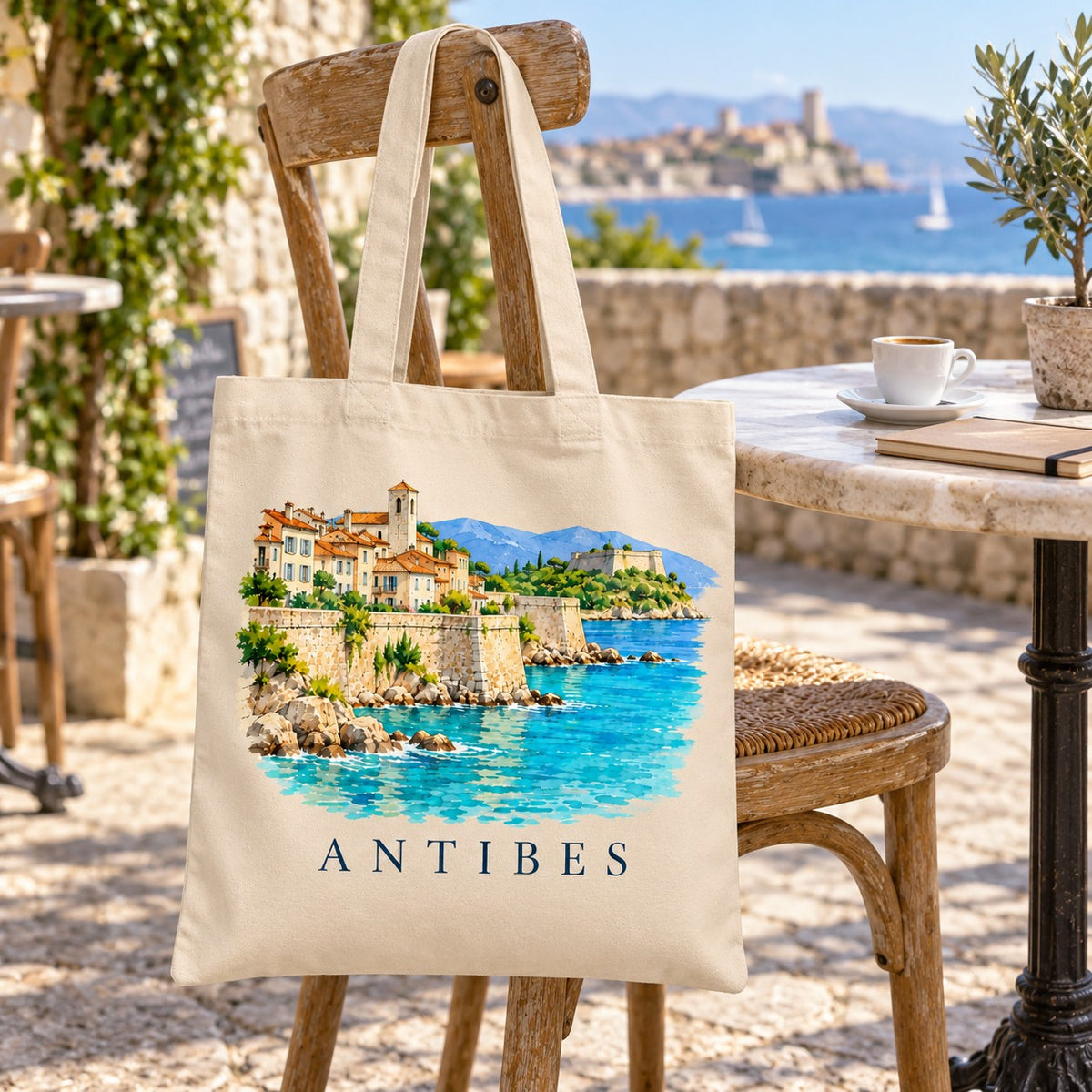 Tote bag Antibes Essentiel suspendu à une chaise en terrasse face à la mer, avec un café