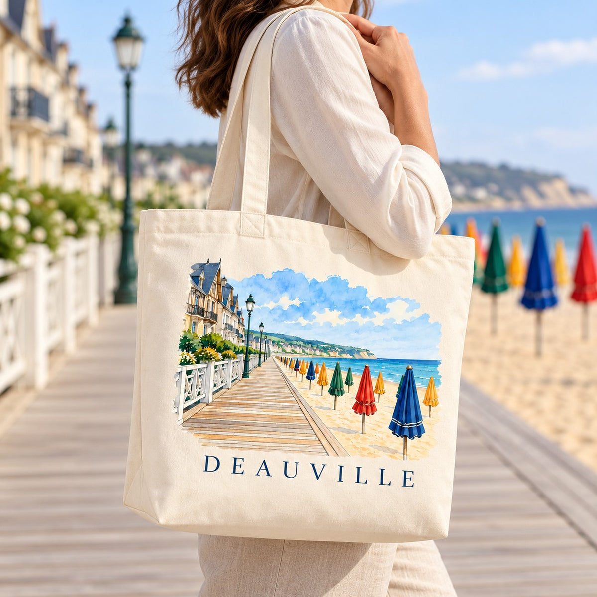 Tote bag Deauville Premium porté à l'épaule sur les Planches, parasols en arrière-plan