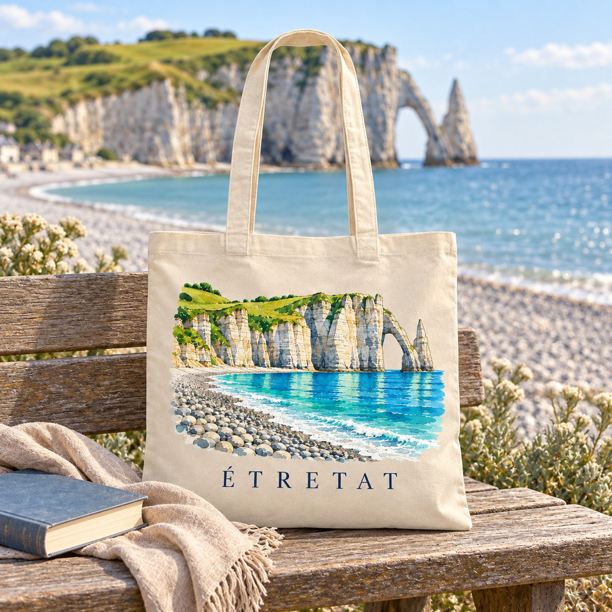 Tote bag Étretat Essentiel posé sur un banc face aux falaises, avec un livre