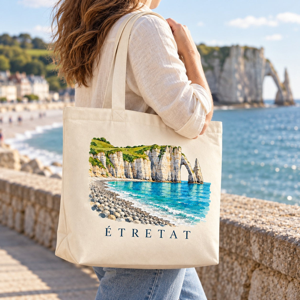 Tote bag Étretat Premium porté à l'épaule sur la promenade, falaises d'Étretat en arrière-plan