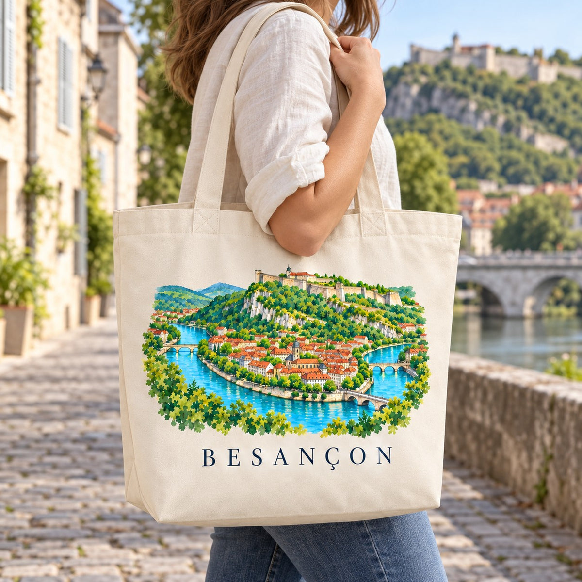 Tote bag Besançon Premium porté à l'épaule sur les quais du Doubs, citadelle en arrière-plan