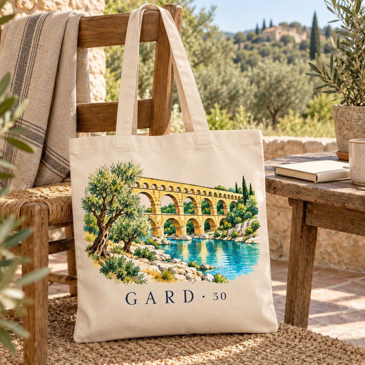 Tote bag Gard (30) Essentiel posé sur une chaise en terrasse face aux collines, avec un livre et un plaid