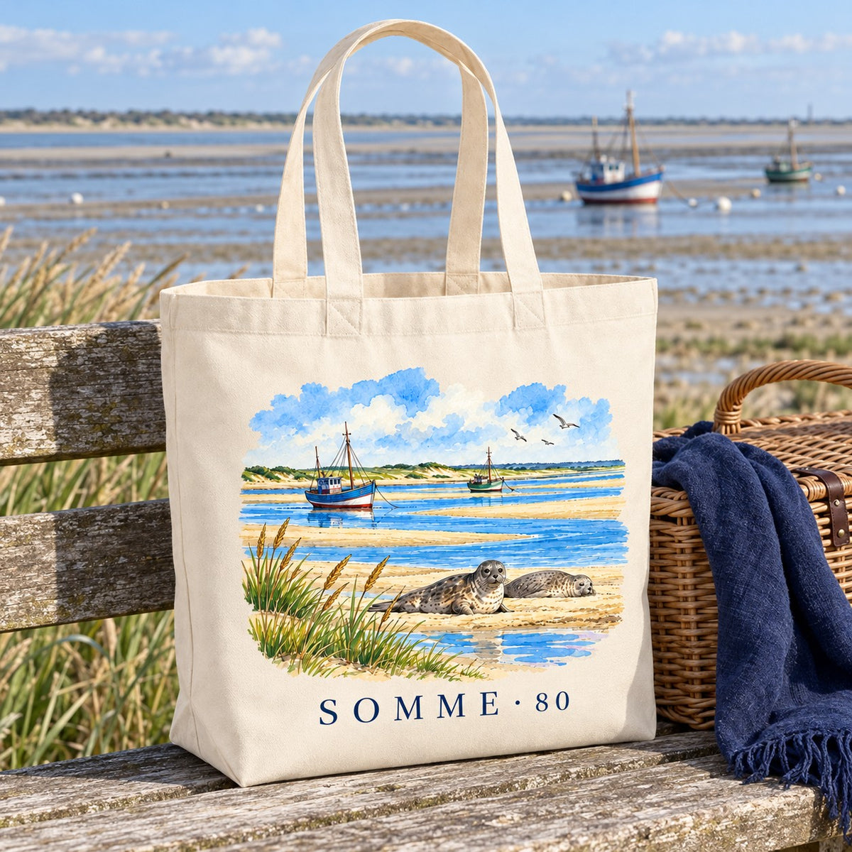 Tote bag Somme (80) Premium posé sur un banc de bois face à la baie, avec un panier et un plaid