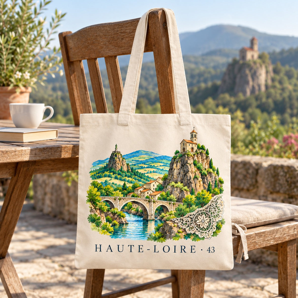 Tote bag Haute-Loire (43) Essentiel suspendu à une chaise en terrasse face aux pitons volcaniques, avec un café