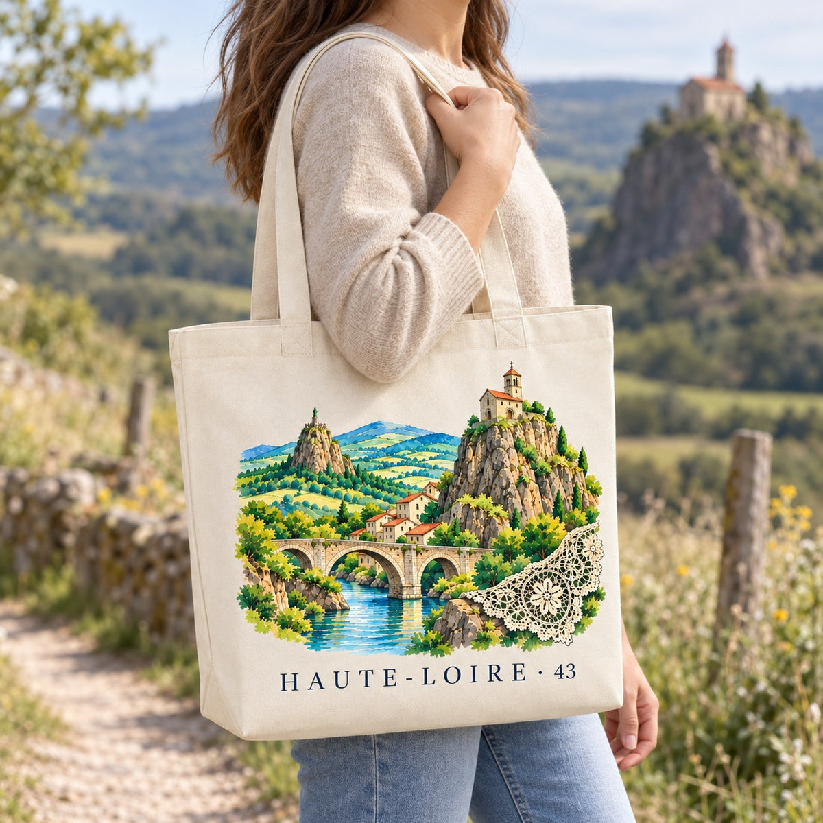 Tote bag Haute-Loire (43) Premium porté à l'épaule sur un sentier, chapelle sur son rocher en arrière-plan