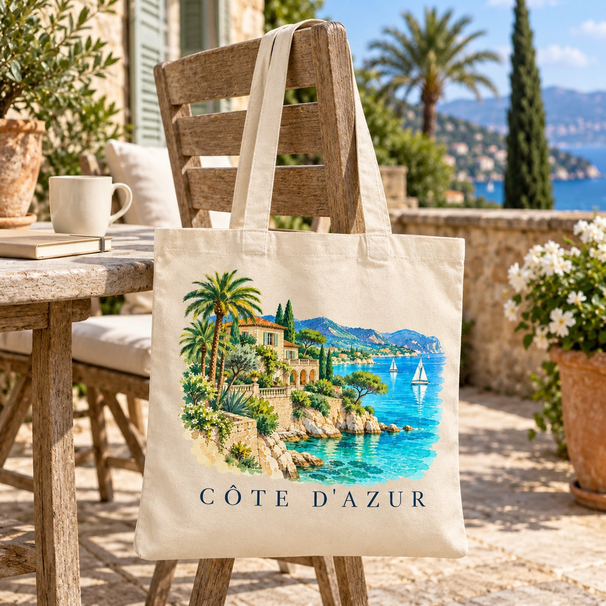 Tote bag Côte d'Azur Essentiel suspendu à une chaise de bois en terrasse face à la mer
