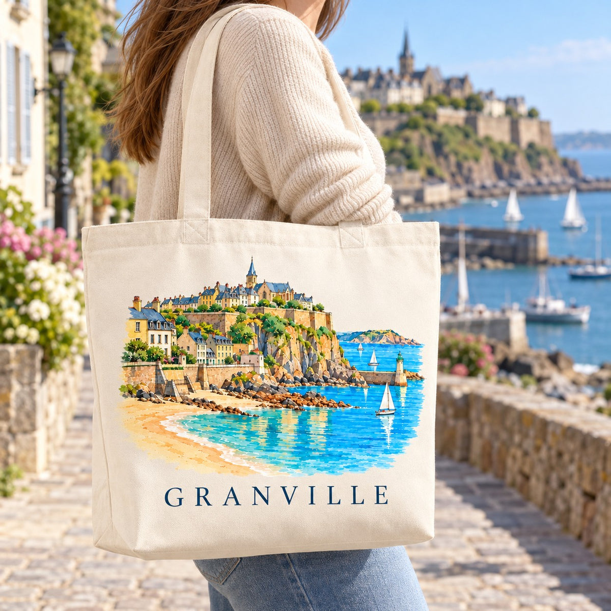 Tote bag Granville Premium porté à l'épaule sur la promenade du bord de mer, haute ville en arrière-plan