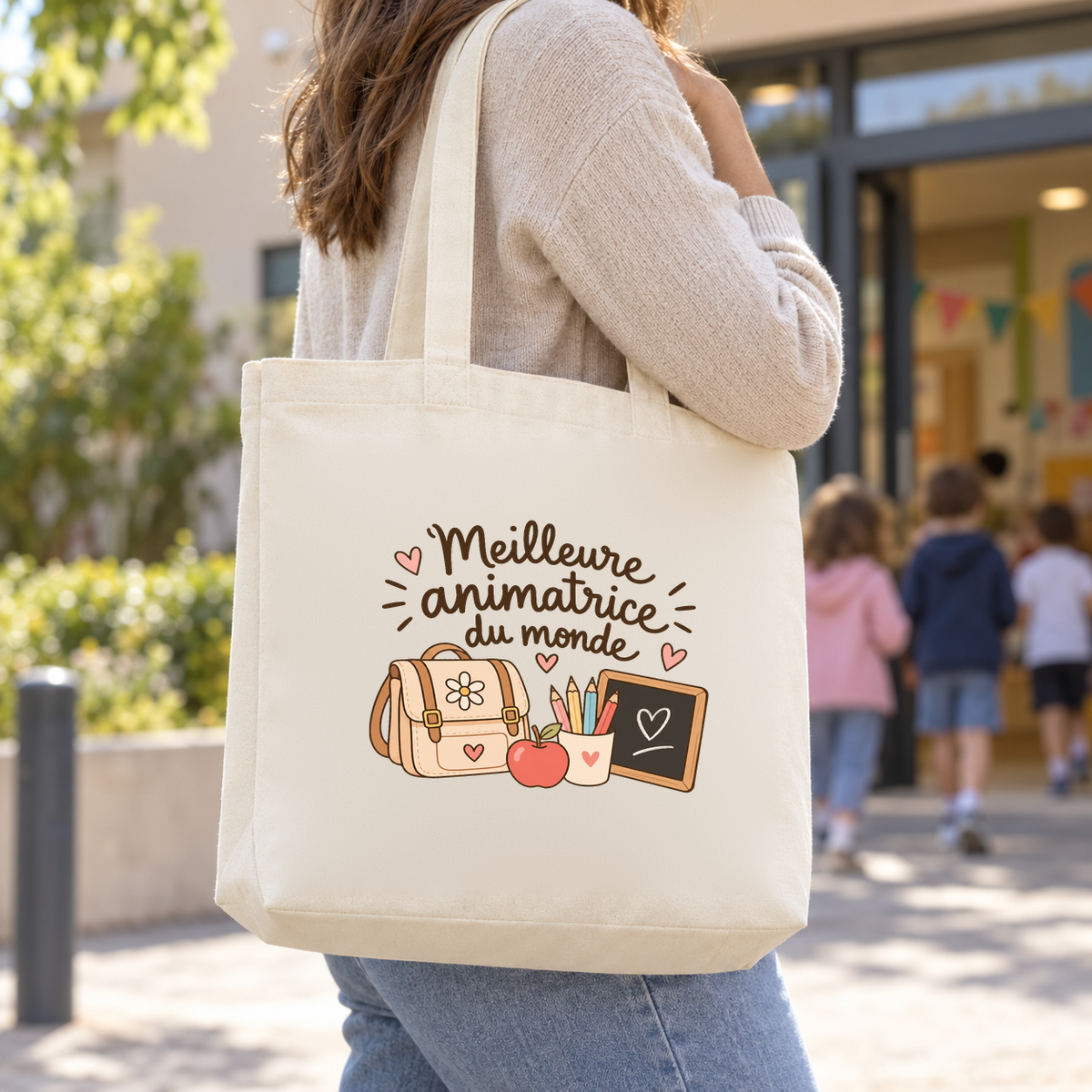 Tote bag animatrice « Meilleure animatrice du monde » Premium porté à l'épaule dans la cour du centre de loisirs, à l'arrivée des enfants