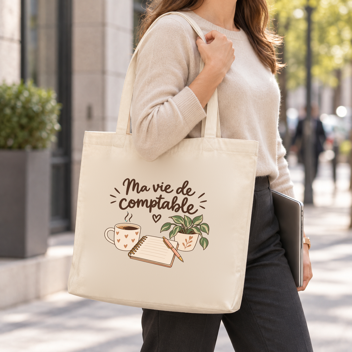 Tote bag comptable « Ma vie de comptable » Premium porté à l'épaule dans la rue, un ordinateur sous le bras