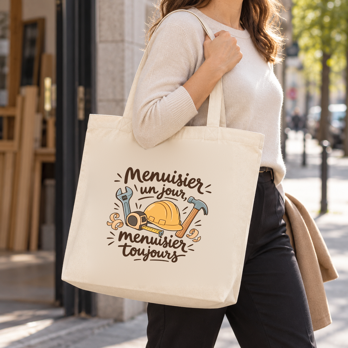 Tote bag menuisier « Menuisier un jour, menuisier toujours » Premium porté à l'épaule devant un atelier de menuiserie