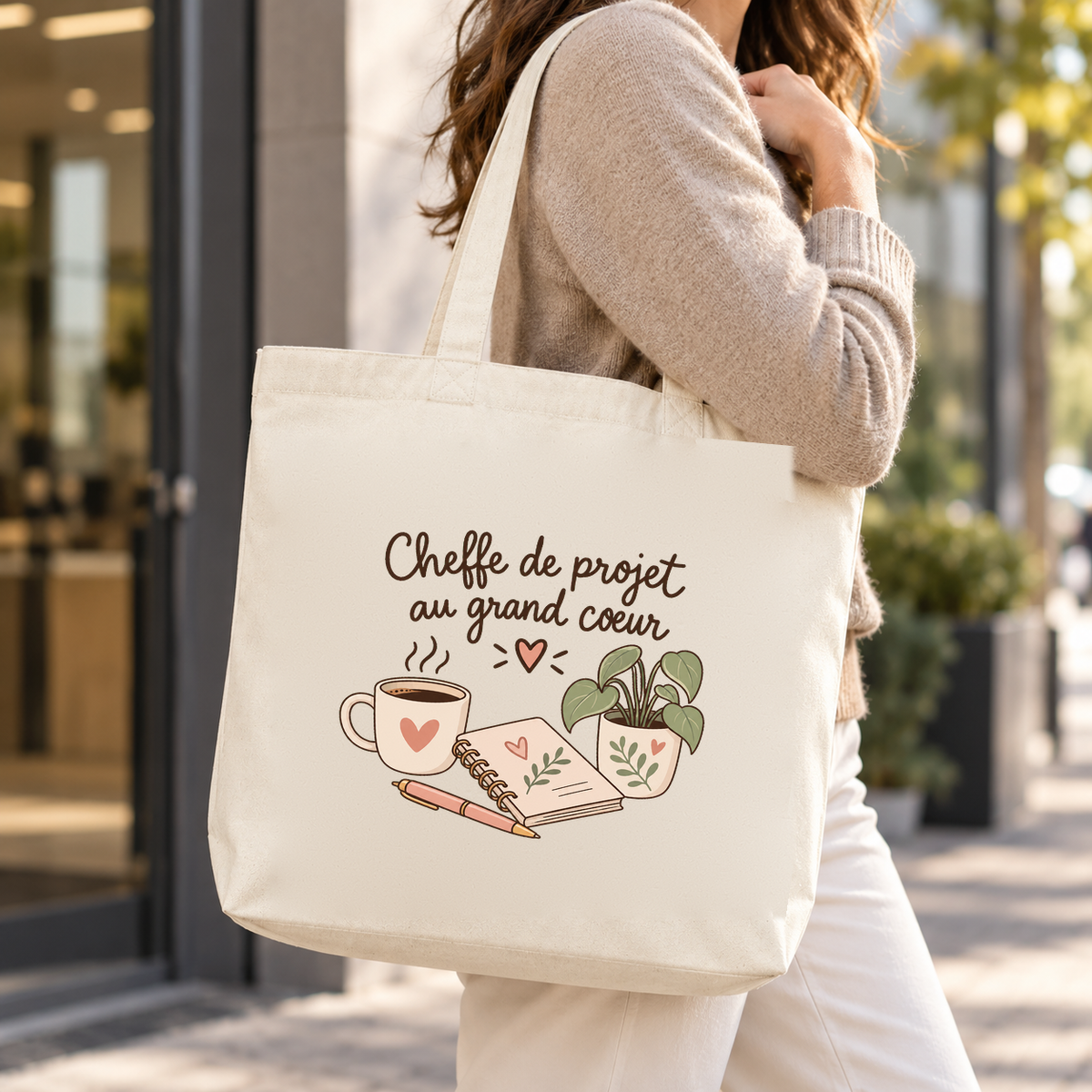 Tote bag cheffe de projet « Cheffe de projet au grand cœur » Premium porté à l'épaule dans la rue, devant une vitrine