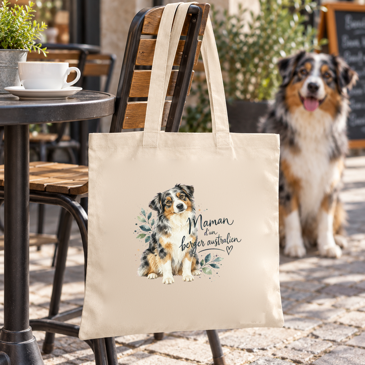 Tote bag berger australien « Maman d'un berger australien » Essentiel suspendu à une chaise de terrasse, à côté d'un berger australien