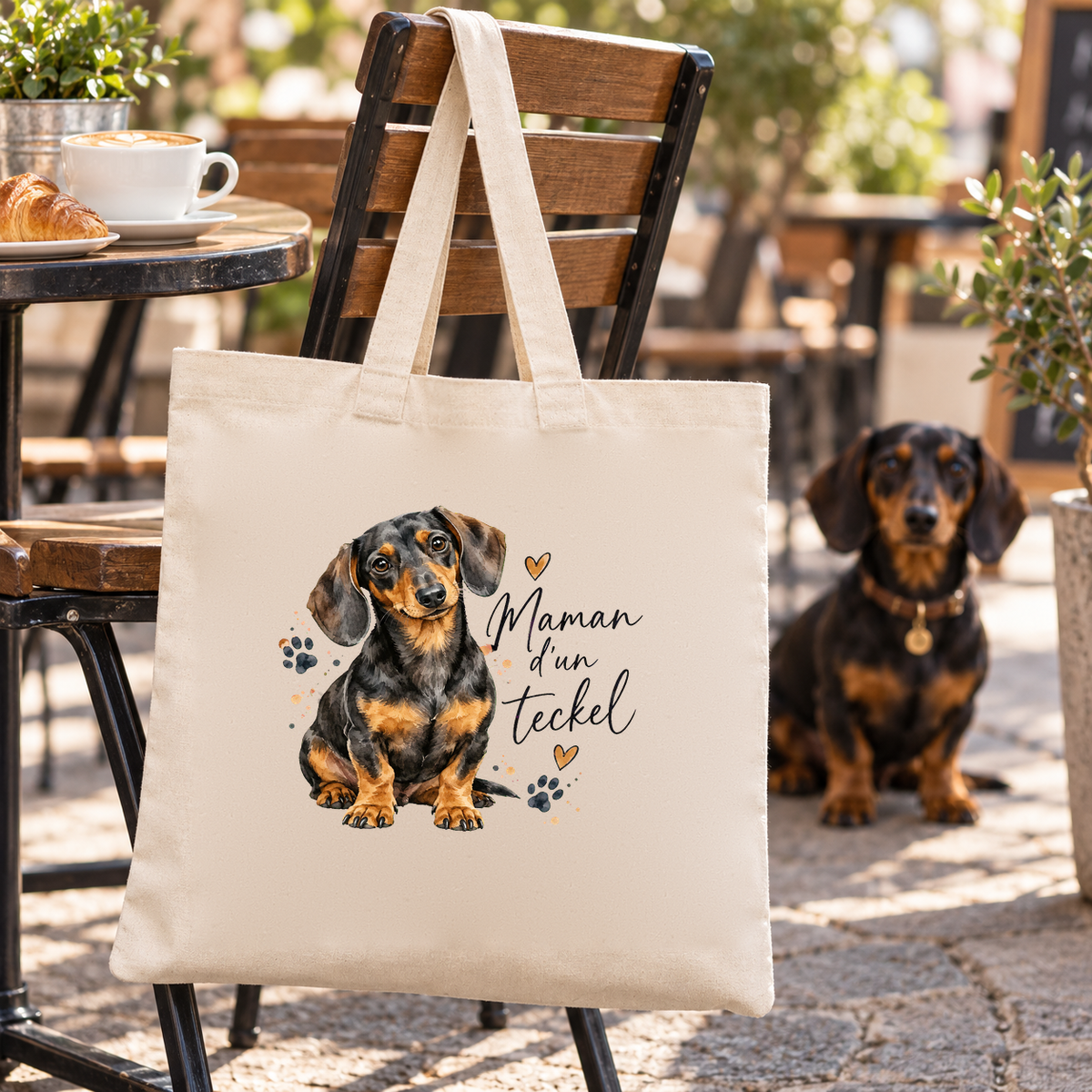 Tote bag teckel « Maman d'un teckel » Essentiel suspendu à une chaise de terrasse, un teckel assis à côté
