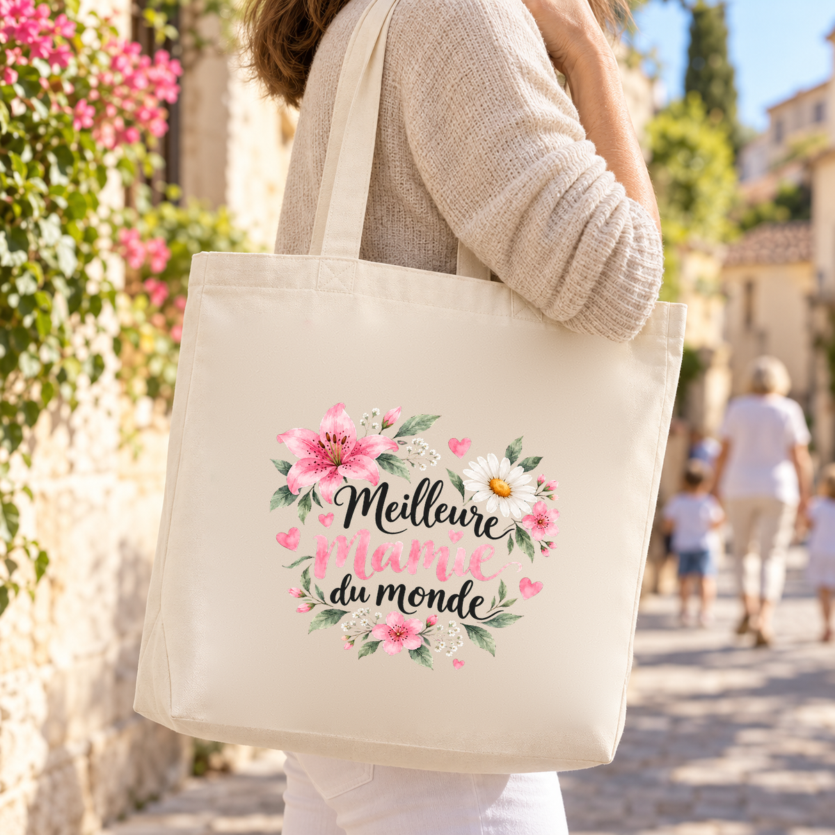 Tote bag mamie « Meilleure mamie du monde » Premium porté à l'épaule dans une ruelle de village fleurie