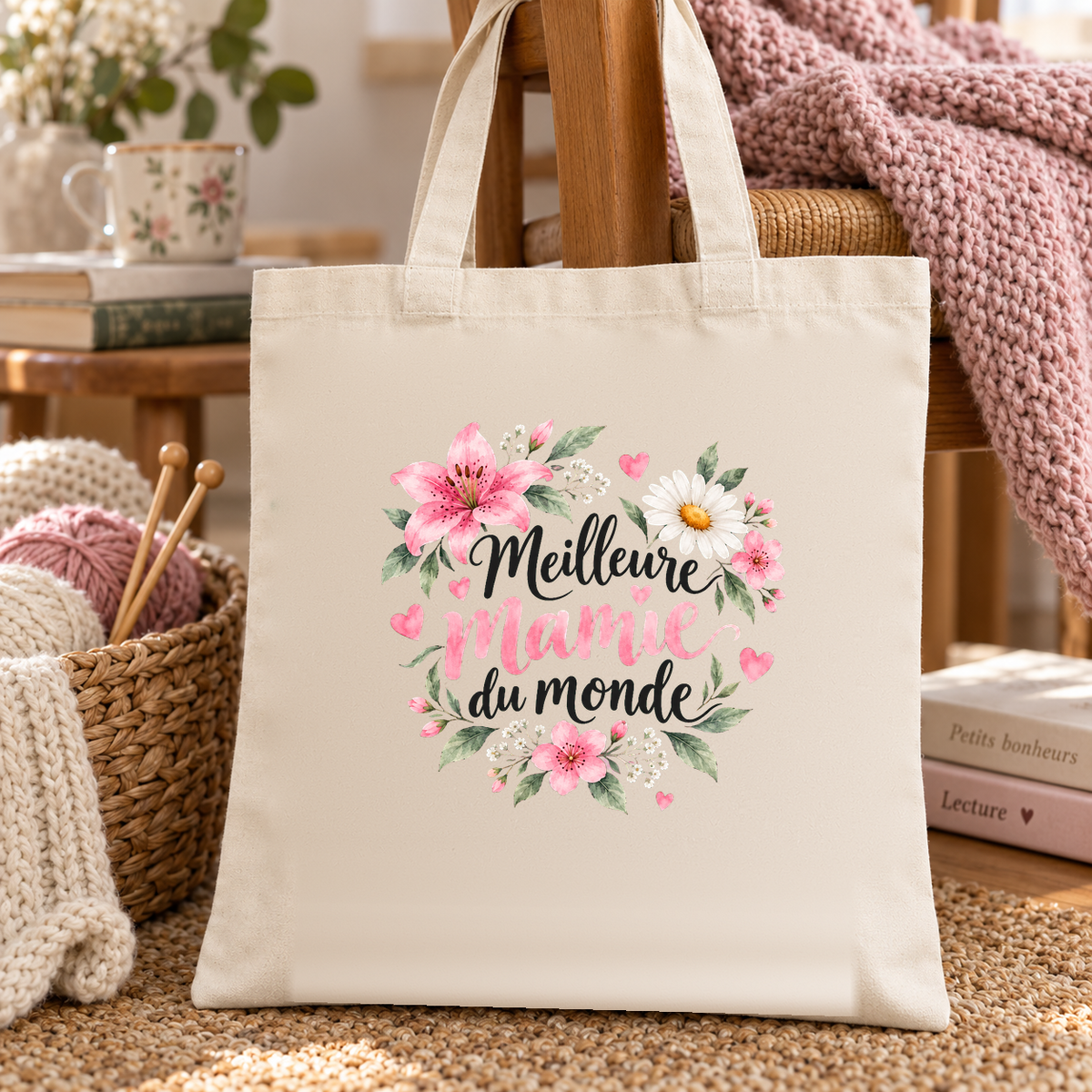 Tote bag mamie « Meilleure mamie du monde » Essentiel posé sur un fauteuil, à côté d'un panier de pelotes et d'aiguilles à tricoter