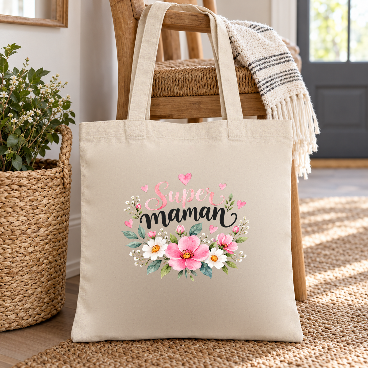 Tote bag maman « Super maman » Essentiel posé au pied d'une chaise, à côté d'un panier en osier